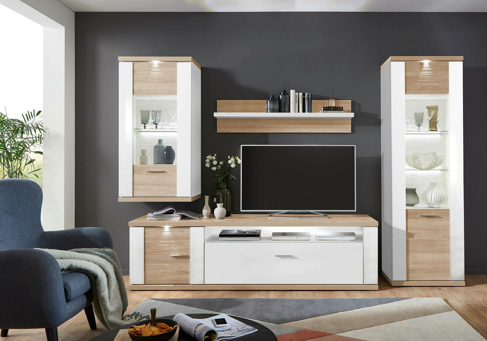 XORA Wandboard MANHATTAN Modernes Wohnzimmer mit Wandboard in Holzoptik, frontal betrachtet, umgeben von stilvollen Vitrinen und einem TV-Schrank.