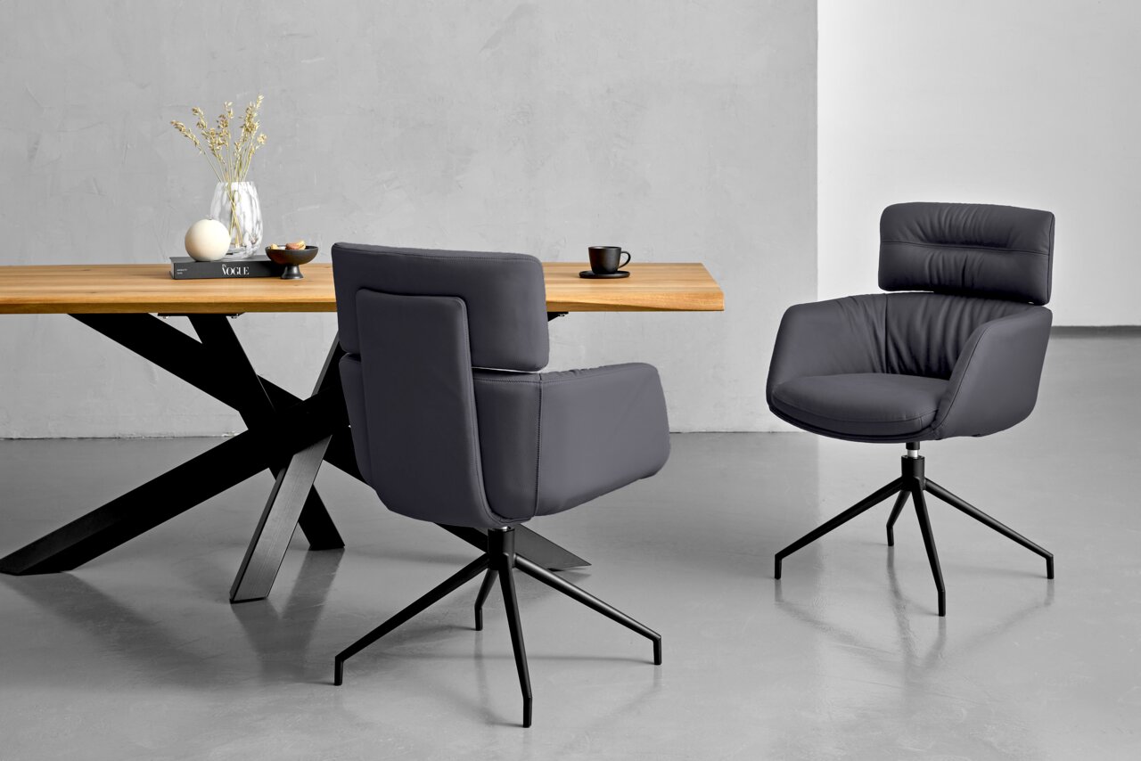 Dieter Knoll Armlehnstuhl PABLO Zwei moderne Armlehnstühle in dunklem Grau mit schwarzem Metallgestell, vor einem Holztisch mit Dekoration, aus seitlicher Perspektive fotografiert.