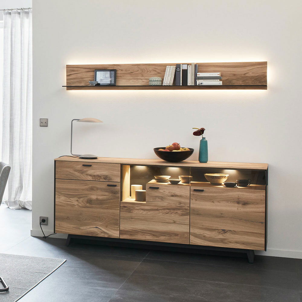 Modernes Wohnzimmer mit beleuchtetem Wandpaneel und Sideboard aus Holz, seitliche Perspektive.