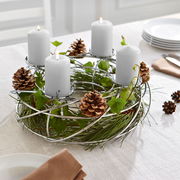 Silberner Dekokranz für 4 Kerzen mit Tannenzapfen und grünen Zweigen, auf einem Tisch arrangiert. Perspektive von schräg oben.