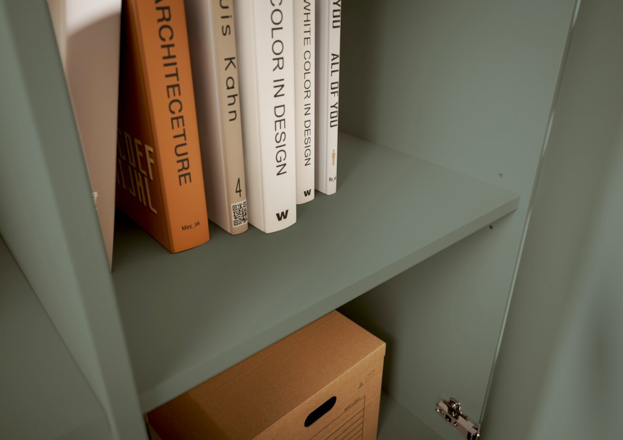 Nahaufnahme eines grünen Regals mit Büchern und einer Kartonbox, seitliche Perspektive.
