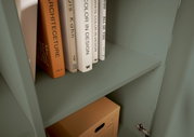 Nahaufnahme eines grünen Regals mit Büchern und einer Kartonbox, seitliche Perspektive.