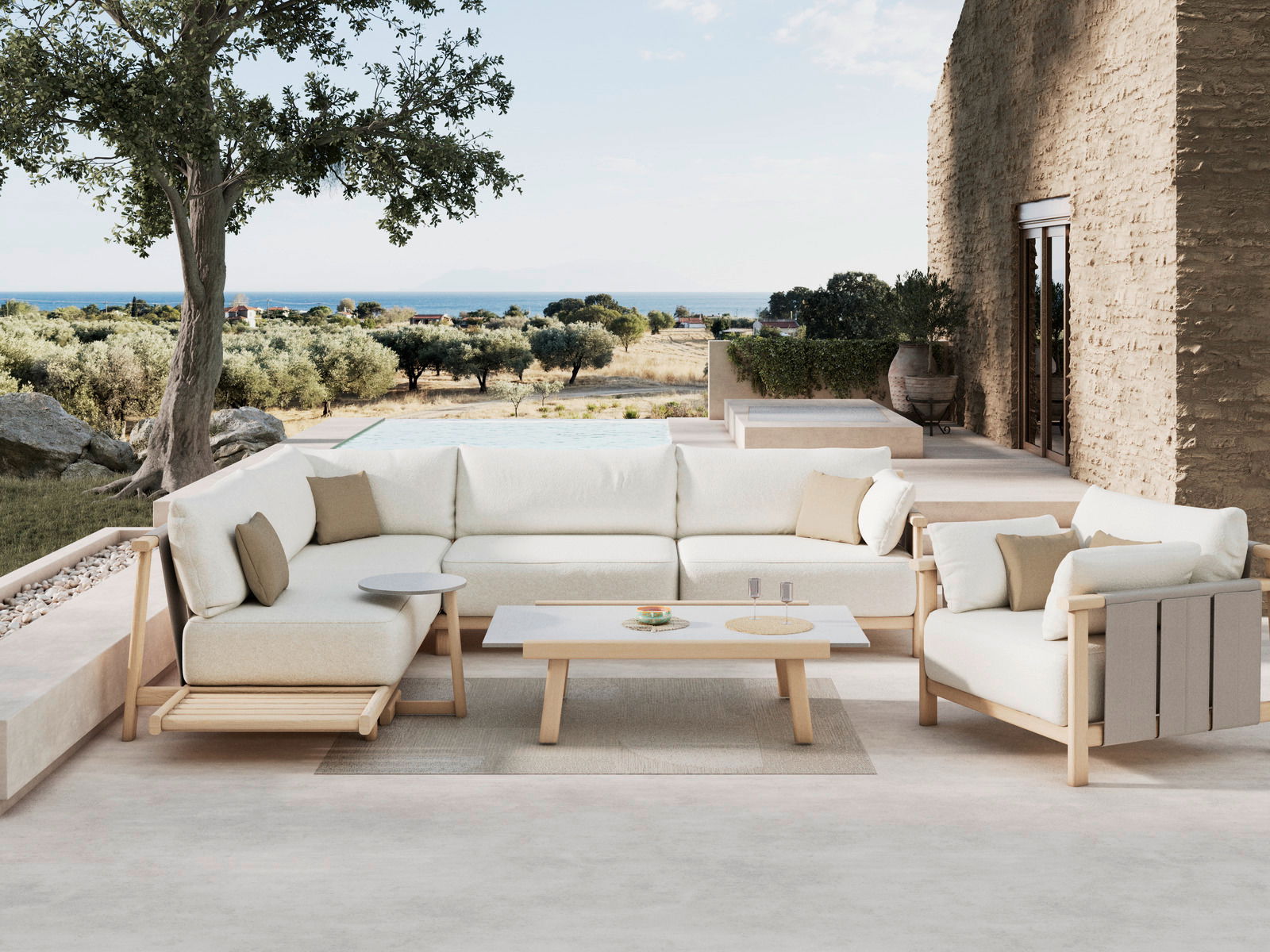 Dieter Knoll Fauteuil MARI Moderne Loungeeckgarnitur mit hellem Holzrahmen und weißen Kissen, umgeben von einem mediterranen Garten mit Blick auf das Meer, aus einer seitlichen Perspektive aufgenommen.