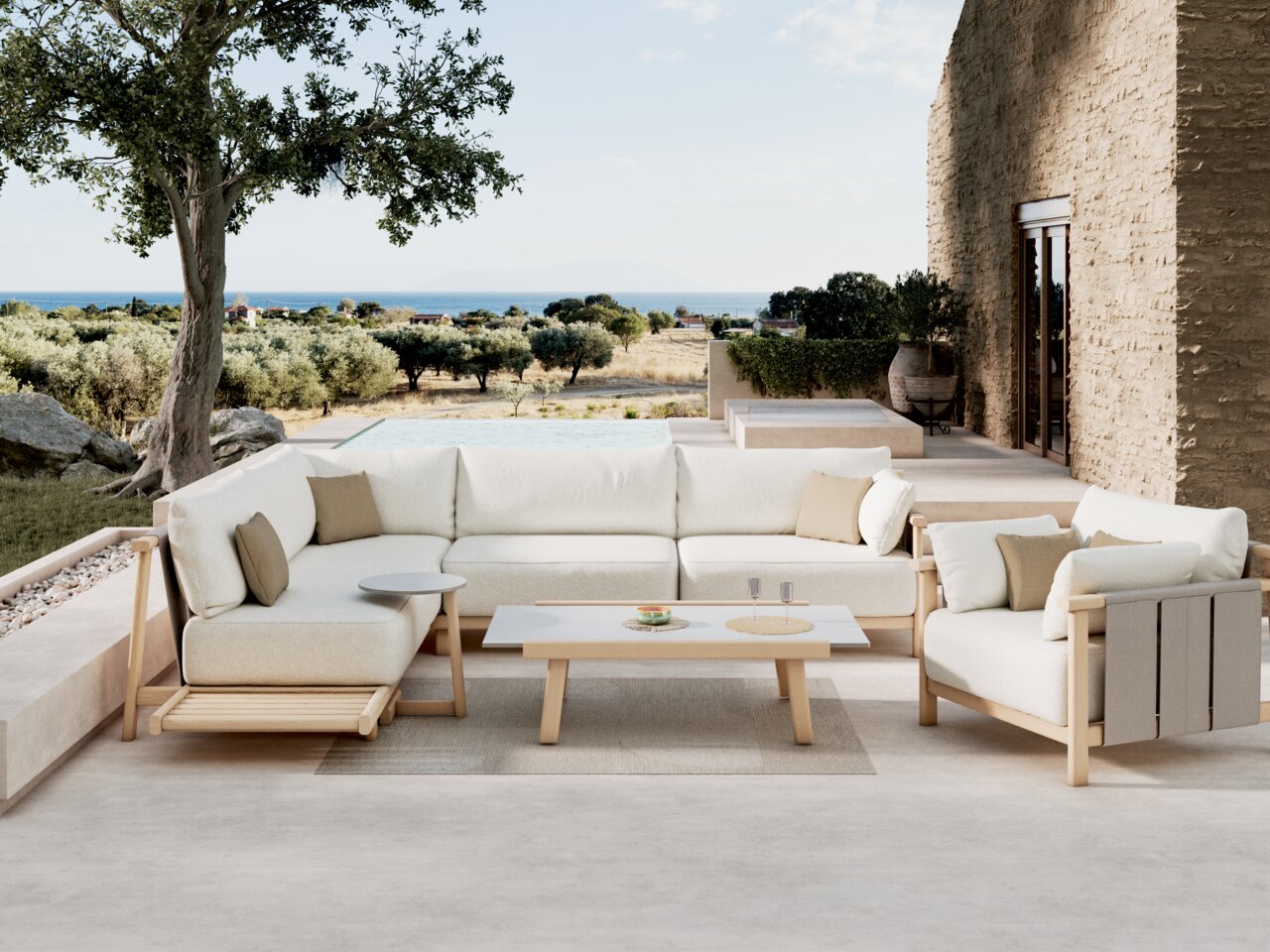 Dieter Knoll Beistelltisch MARI Moderne Loungeeckgarnitur mit hellem Holzrahmen und weißen Kissen, umgeben von einem mediterranen Garten mit Blick auf das Meer, aus einer seitlichen Perspektive aufgenommen.