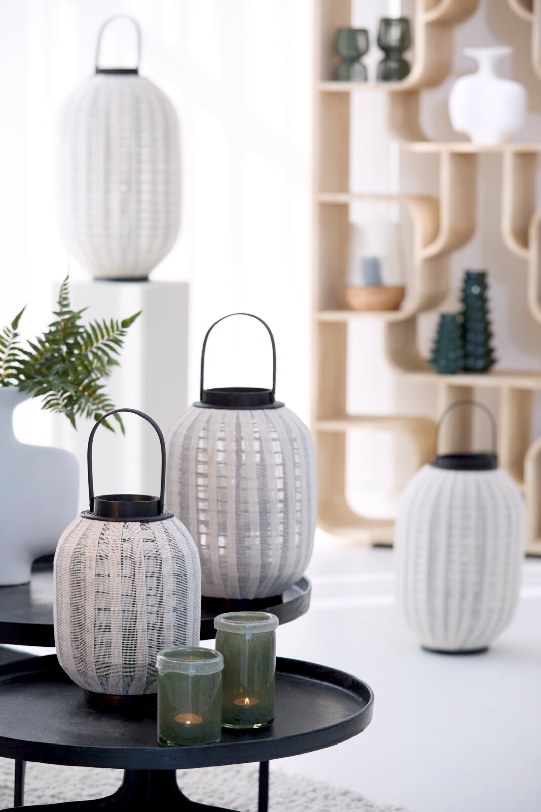 Vooraanzicht op een stijlvolle set witte, ovaalvormige lantaarns met geweven structuur en zwarte metalen hengsels in een modern interieur.