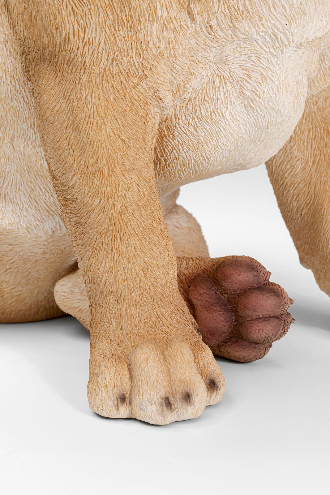 Nahaufnahme der Pfoten einer Deko-Figur eines Hundes, die detaillierte Fellstruktur und die Vorderansicht der Figur zeigend.