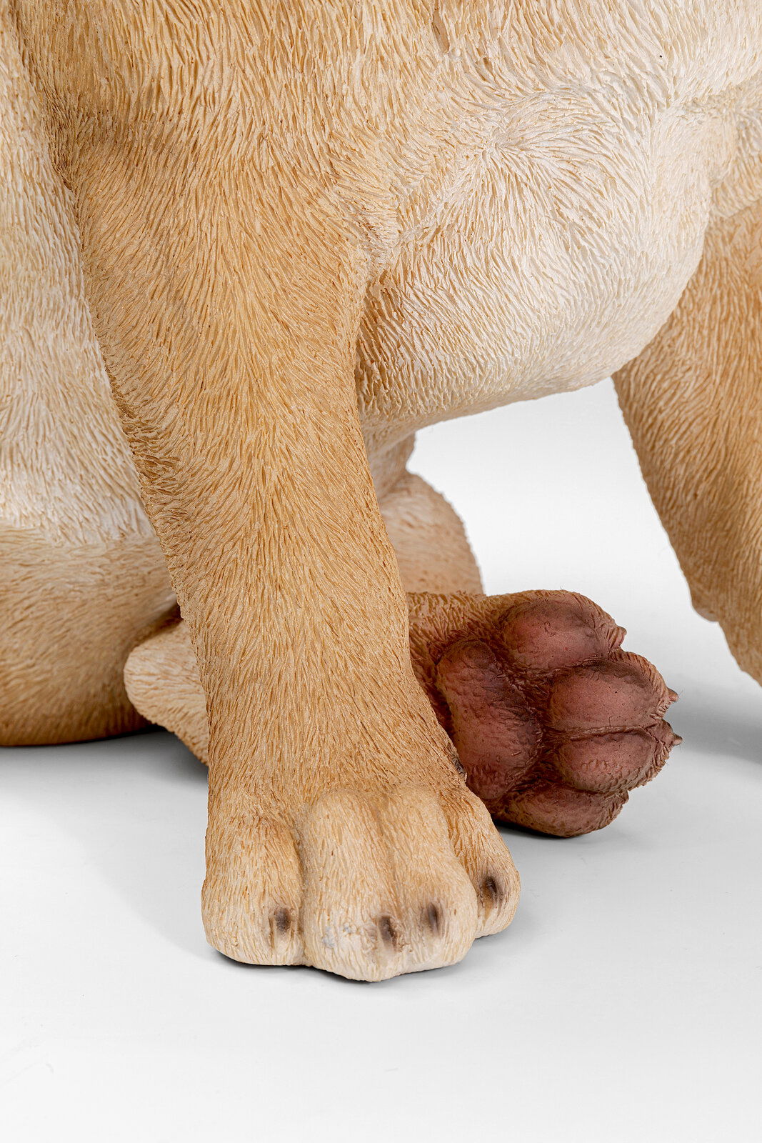 Nahaufnahme der Pfoten einer Deko-Figur eines Hundes, die detaillierte Fellstruktur und die Vorderansicht der Figur zeigend.