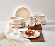 Tafelservice 8-tlg. in beige, bestehend aus Tellern, Schalen und Tassen, auf einem Tisch mit Dekorationen, aus seitlicher Perspektive fotografiert.