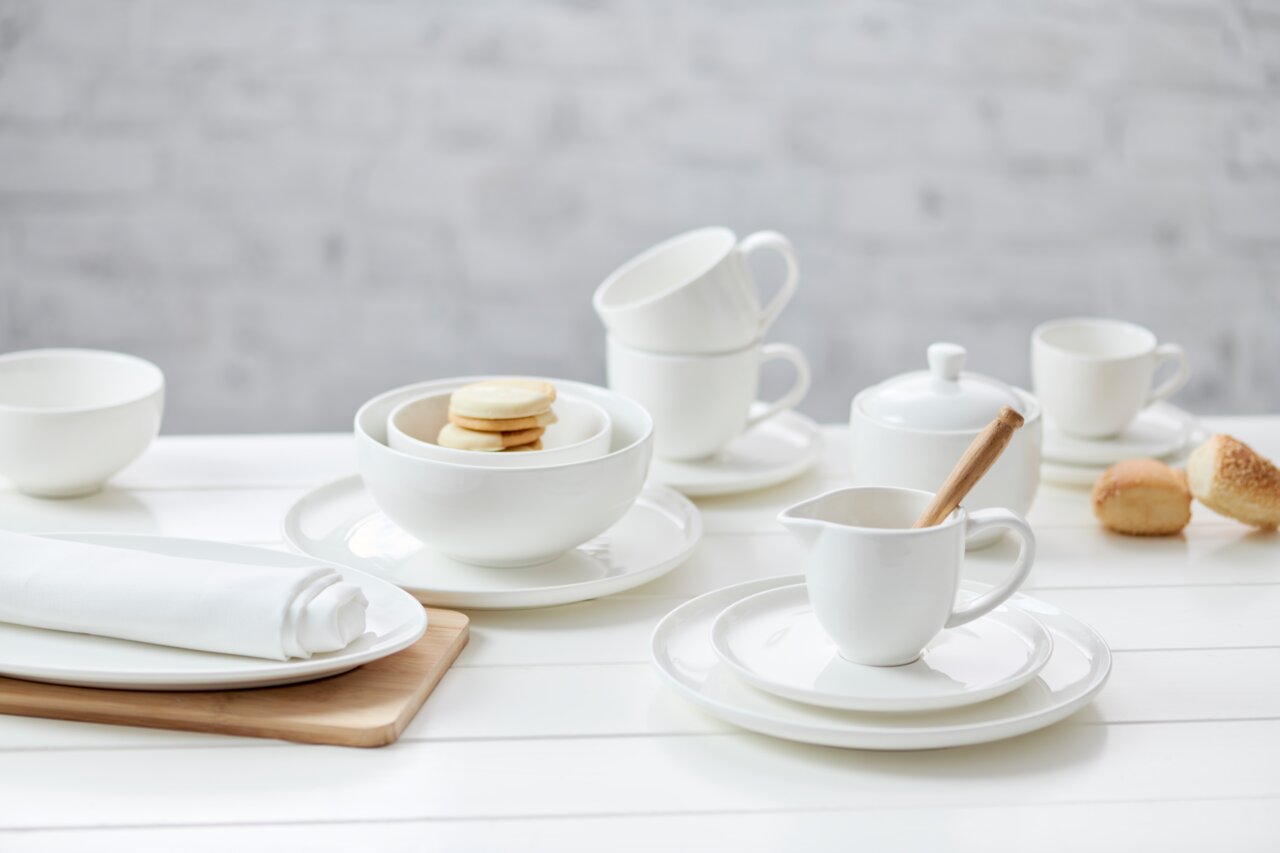 Elegante Espressountertasse Skagen 11cm aus weißem Porzellan, präsentiert in einer stilvollen Tischdekoration mit weiteren Geschirrteilen, aus der Vogelperspektive.