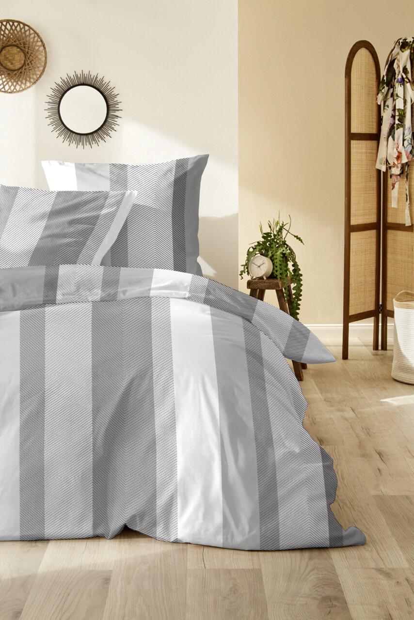 Grau-weiß gestreifte Bettwäsche mit Kissenbezug und Deckenbezug auf einem gemachten Bett, frontal in leichter Schrägansicht im Schlafzimmer fotografiert.