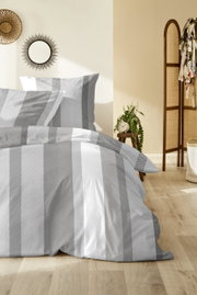 Grau-weiß gestreifte Bettwäsche mit Kissenbezug und Deckenbezug auf einem gemachten Bett, frontal in leichter Schrägansicht im Schlafzimmer fotografiert.