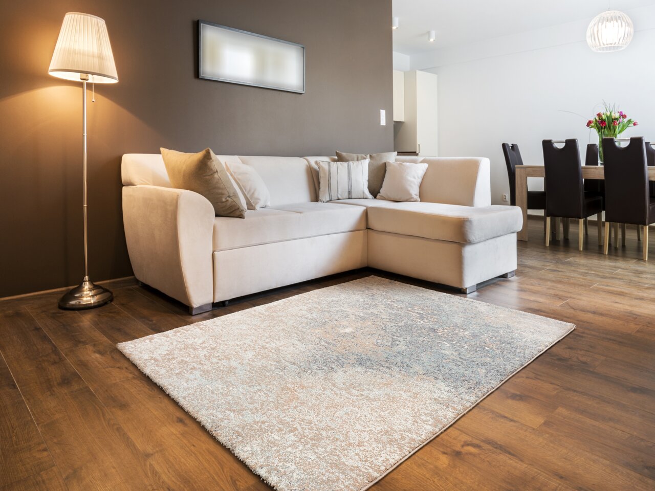 Designer Teppich in einem modernen Wohnzimmer mit beiger Couch und Stehlampe, aus der Perspektive des Bodens aufgenommen.