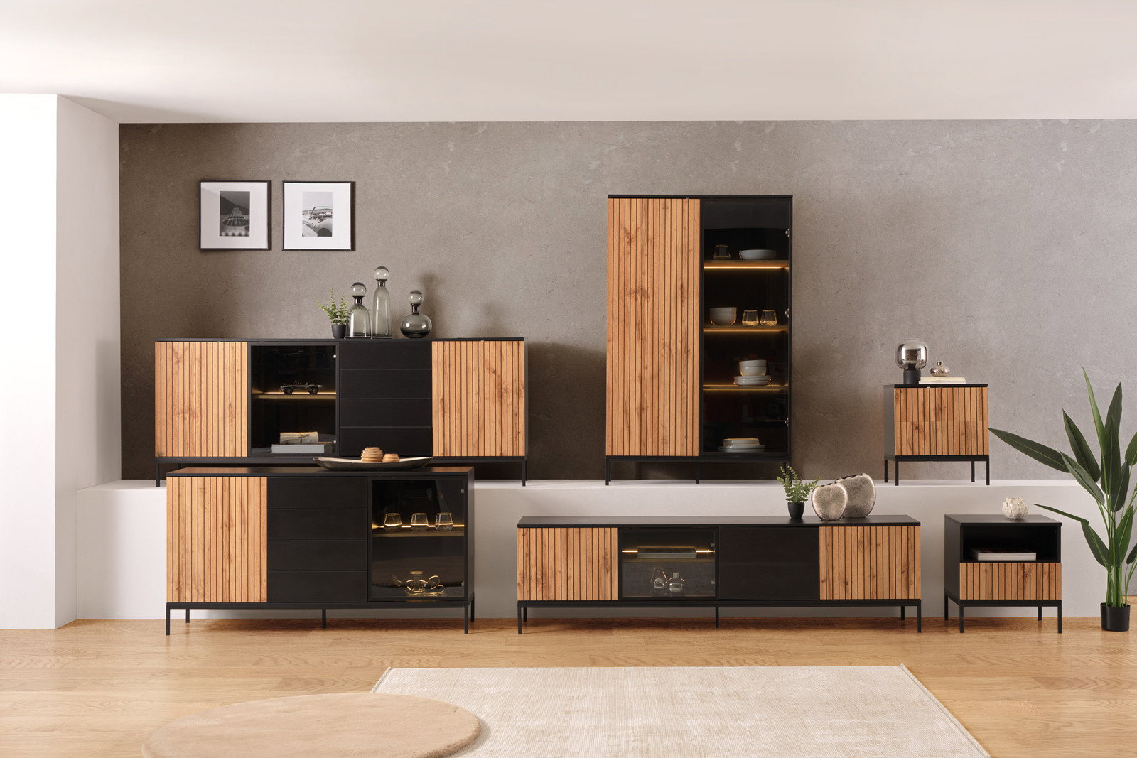 Moderne Wohnzimmermöbel mit Holz- und Schwarzelementen, bestehend aus Highboard, TV-Lowboard, XL-TV-Lowboard, XL-Sideboard, Sideboard und Nachtkommoden, aus frontaler Perspektive.