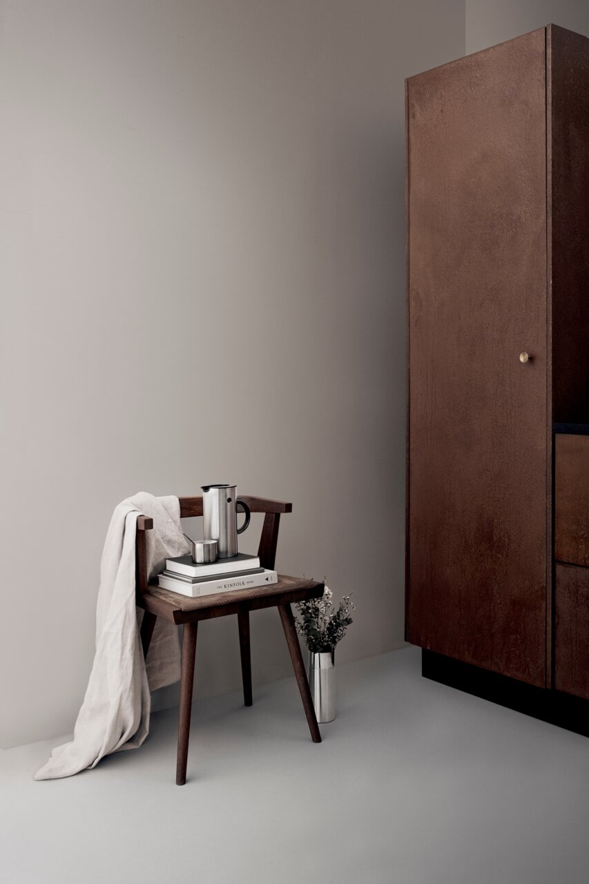 Isolierkanne aus Stahl mit 0,5 Liter Fassungsvermögen, auf einem Stuhl mit Büchern und Tuch, seitliche Perspektive