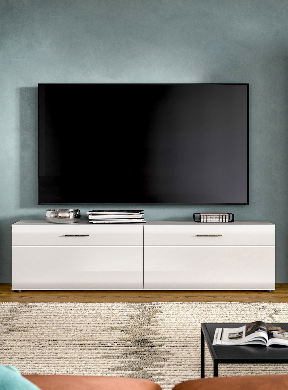 Modernes Wohnzimmer mit großem, wandmontiertem Flachbildfernseher über einem weißen Lowboard mit Schubladen; frontale Perspektive.