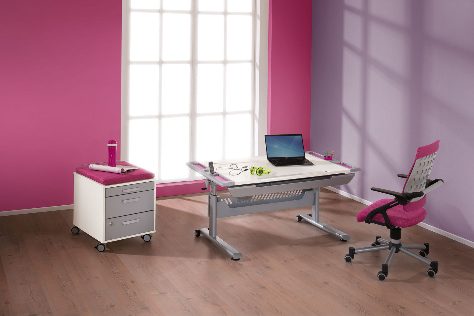 Moderner Schreibtisch in einem hellen Raum mit pinken und lila Wänden, ausgestattet mit einem Laptop, Kopfhörern und Schreibutensilien. Perspektive: seitliche Ansicht.