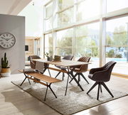 Moderner Esstisch aus Holz mit Metallbeinen, umgeben von stilvollen Stühlen und einer Bank, in einem hellen Raum mit großen Fenstern und Blick auf die Natur. Perspektive von der Seite.
