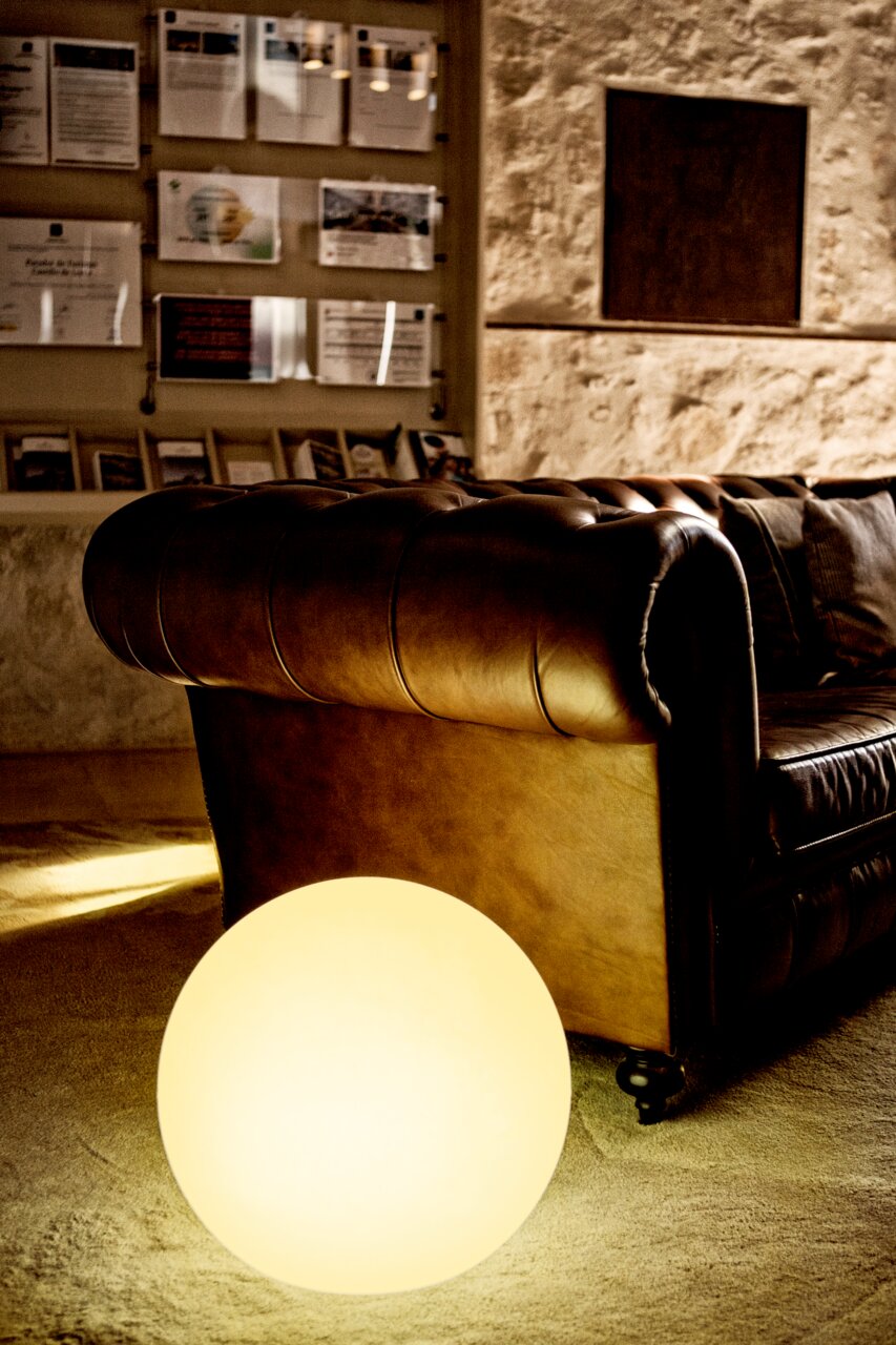 Bruine Chesterfield-lederen bank in een gezellige lounge, op de voorgrond een stralende bolvormige lamp op de vloer; perspectief: close-up van opzij op de armleuning en de zitting