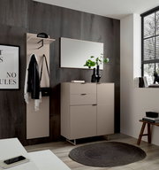 Modernes Flur-Set mit beigem Sideboard, Garderobenpaneel mit Hutablage und Haken sowie Wandspiegel vor dunkler Wand, frontal in leichter Seitenperspektive aufgenommen.