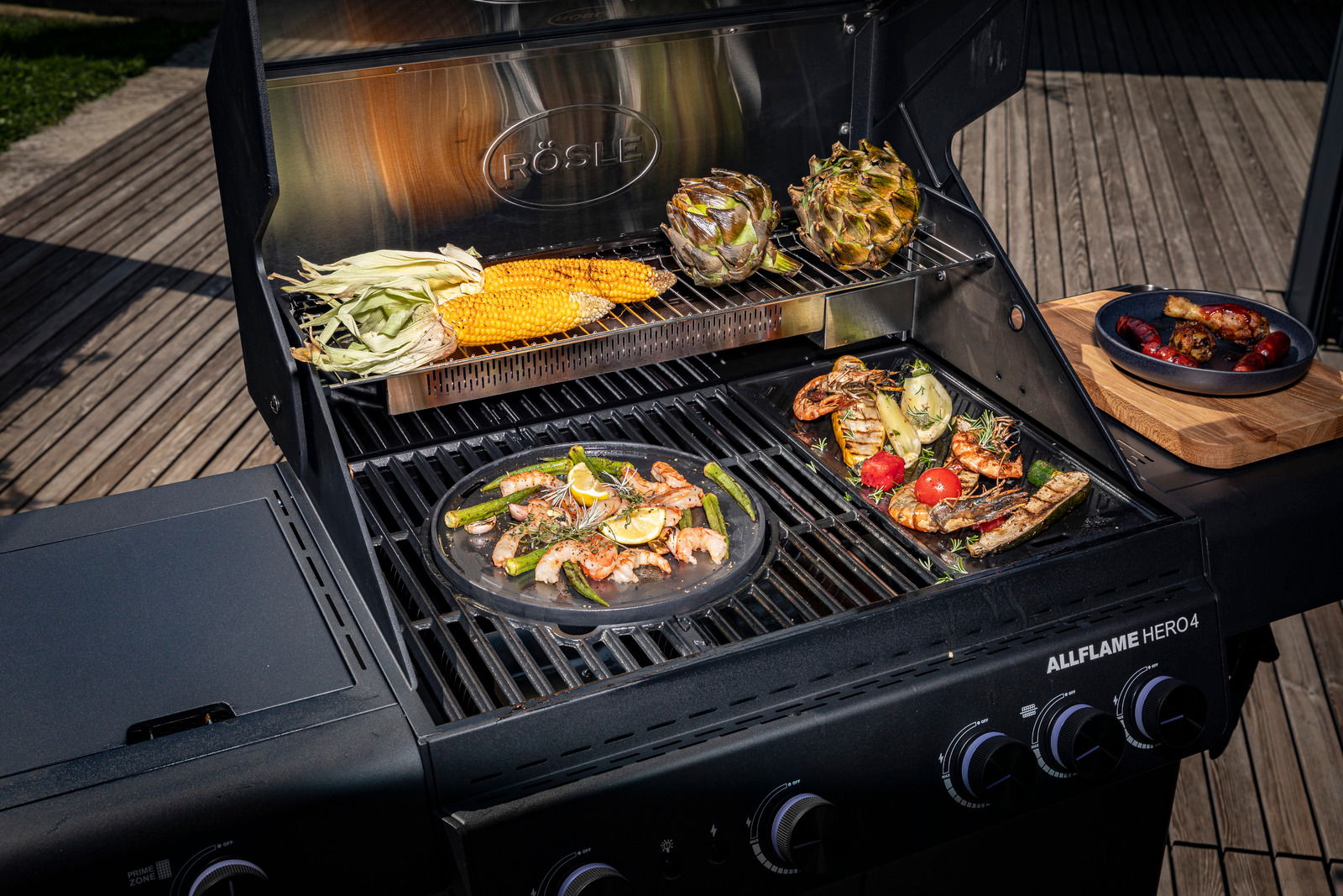 Gasgrill Allflame Hero 4 mit geöffneter Haube, von oben fotografiert, mit gegrilltem Gemüse und Meeresfrüchten auf dem Grillrost.