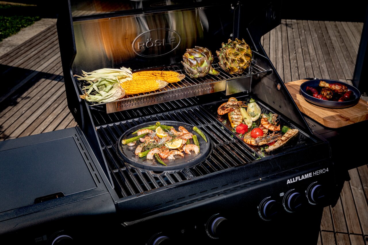 Allflame Hero 4-gasbarbecue met geopende deksel, gefotografeerd van bovenaf, met gegrilde groenten en zeevruchten op het rooster.