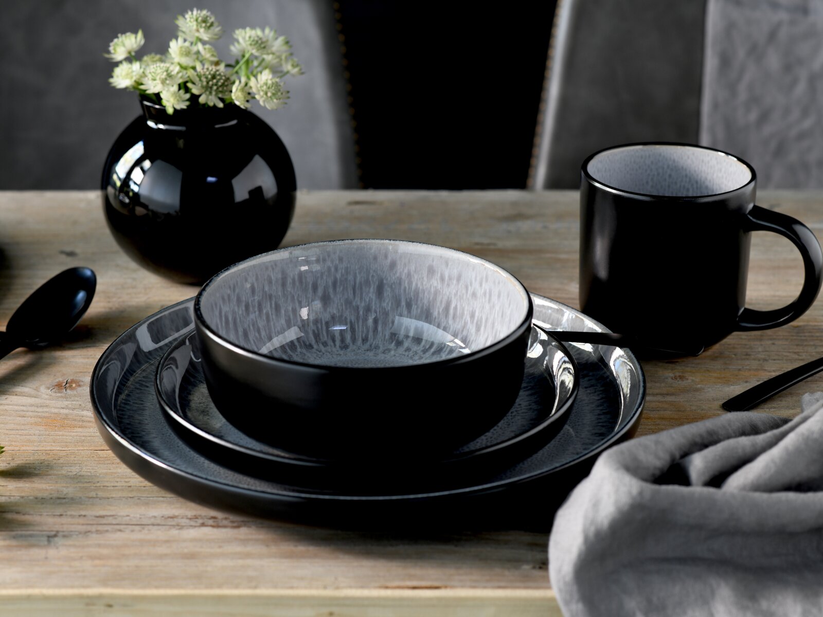 Modernes Keramik-Geschirrset in Schwarz und Grau mit Schale auf zwei Tellern und passender Tasse auf Holztisch, seitliche Perspektive in leicht schräger Ansicht
