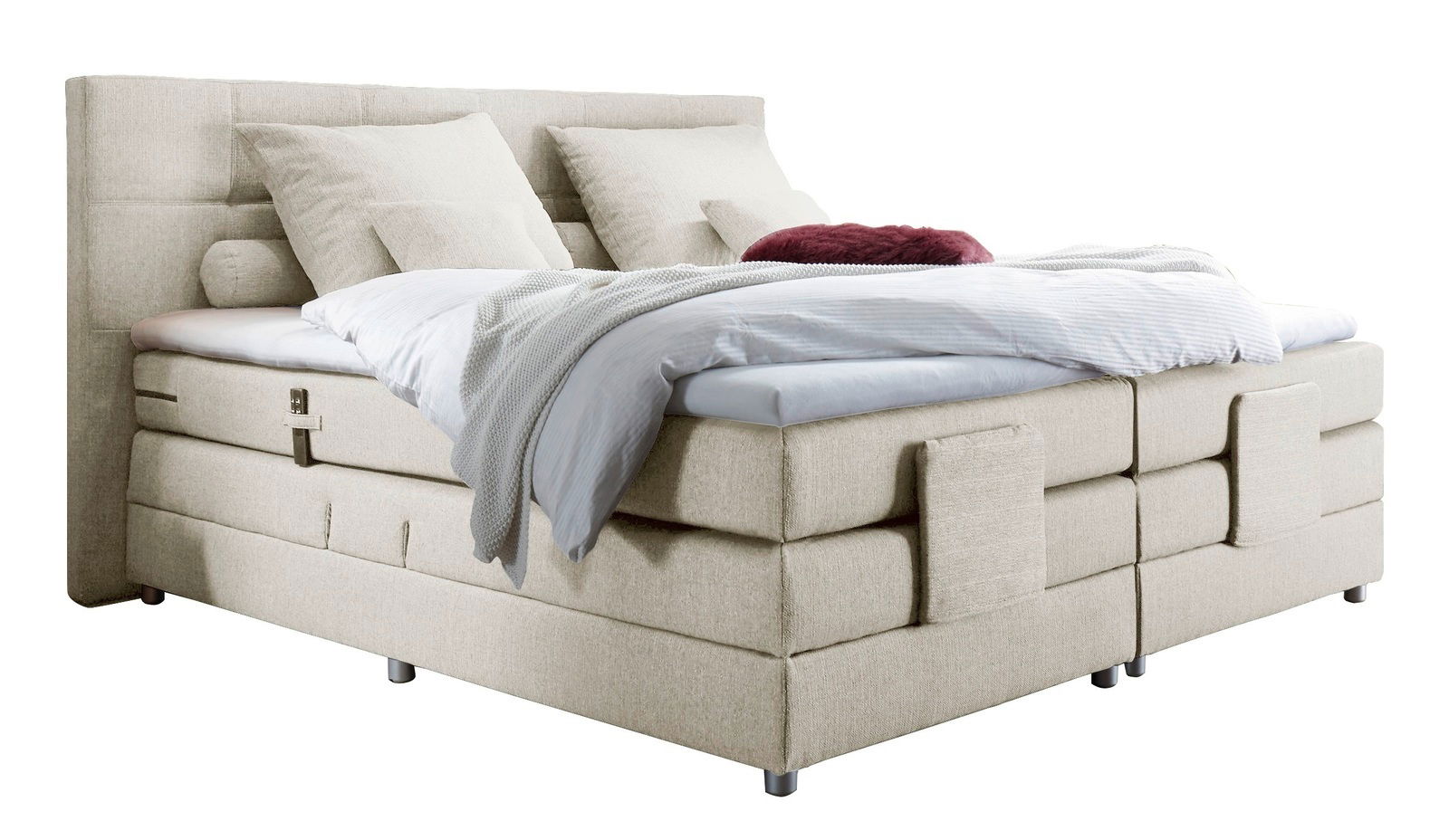 Beiges Boxspringbett mit Kopfteil, seitlicher Perspektive, dekoriert mit Kissen und Decken.