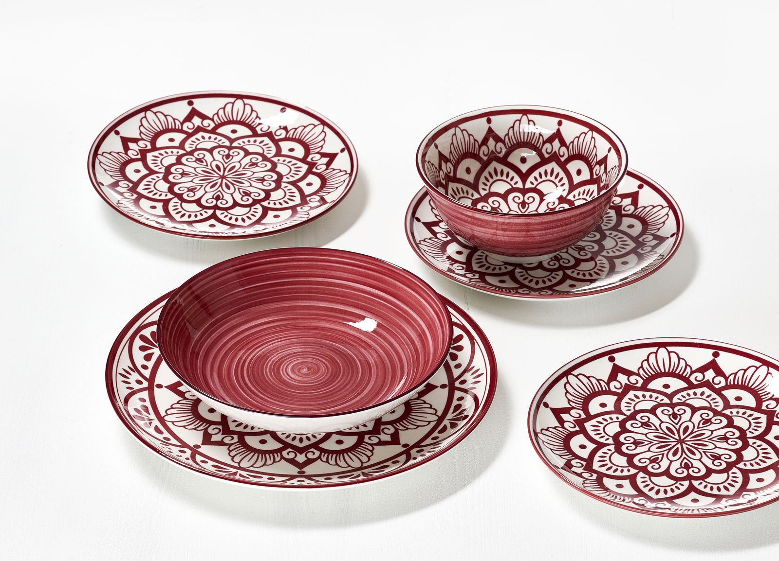 Vogelperspektive auf ein 16-teiliges Tellerset in Burgund mit dekorativen Mustern.