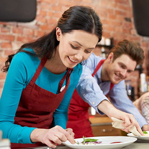 Eine Kochschülerin und ein Kochschüler, die Ihre Teller anrichten.