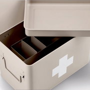 Beige Medizinbox mit abnehmbarem Deckel und Fächern, von oben betrachtet, mit weißem Kreuz auf der Seite.