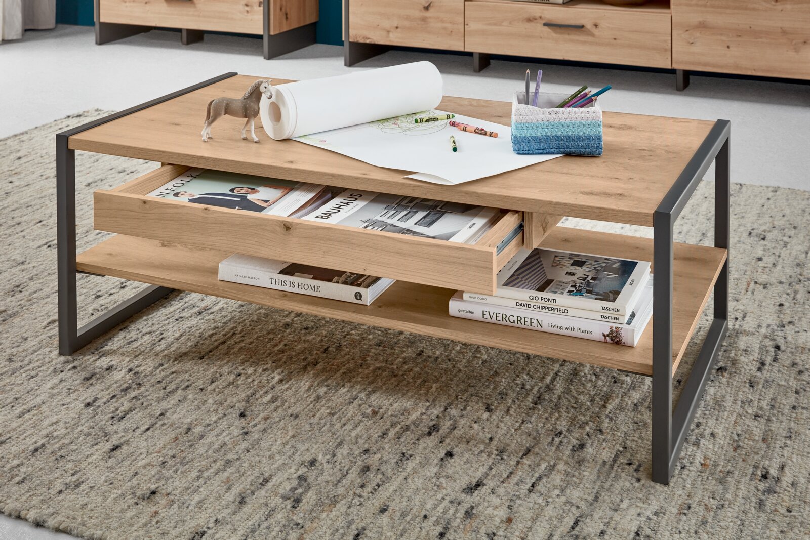 Moderne houten salontafel met metalen frame, gefotografeerd vanuit een schuine hoek van bovenaf, met opbergvakken en decoraties zoals boeken en pennen.