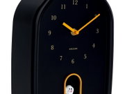 Schwarze Wanduhr mit goldenen Zeigern und Ziffern, seitliche Perspektive, mit kleinem weißen Vogel in einer Öffnung unten.