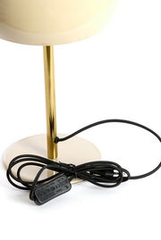 Nahaufnahme einer Tischleuchte mit einem goldenen Ständer und einem schwarzen Kabel auf weißem Hintergrund.