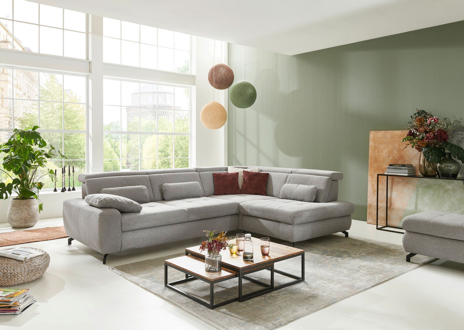 Graue Eckgarnitur in modernem Wohnzimmer mit großen Fenstern, von vorne betrachtet.