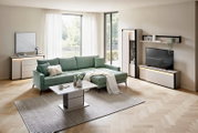 Moderne woonkamer met groene ribstof hoekbank, witte salontafel en tv-meubel met wandplank en vitrinekast, gefotografeerd in frontaal licht schuin perspectief