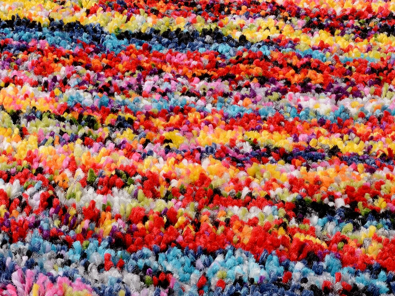 Nahaufnahme eines bunten, flauschigen Teppichs mit einem lebendigen Muster aus roten, blauen, gelben und anderen Farben.