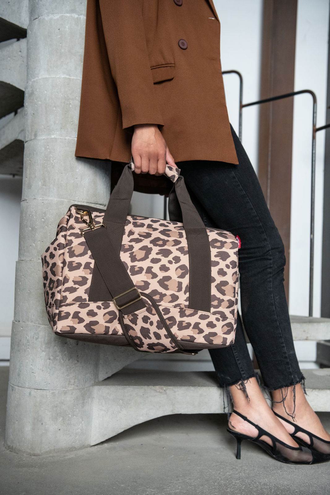 Reisenthel Allrounder M LEO MACCHIATO Leopardenmuster-Tasche in Macchiato-Farbe, getragen von einer Person in einem braunen Blazer und schwarzen Jeans, seitliche Perspektive.