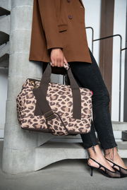 Leopardenmuster-Tasche in Macchiato-Farbe, getragen von einer Person in einem braunen Blazer und schwarzen Jeans, seitliche Perspektive.