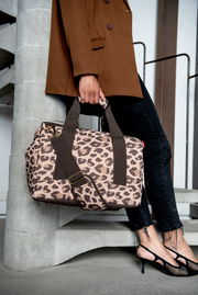 Leopardenmuster-Tasche in Macchiato-Farbe, getragen von einer Person in einem braunen Blazer und schwarzen Jeans, seitliche Perspektive.