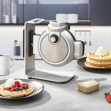 Waffelautomat in moderner Küche, seitliche Perspektive, mit frischen Waffeln und Beeren auf einem Teller.