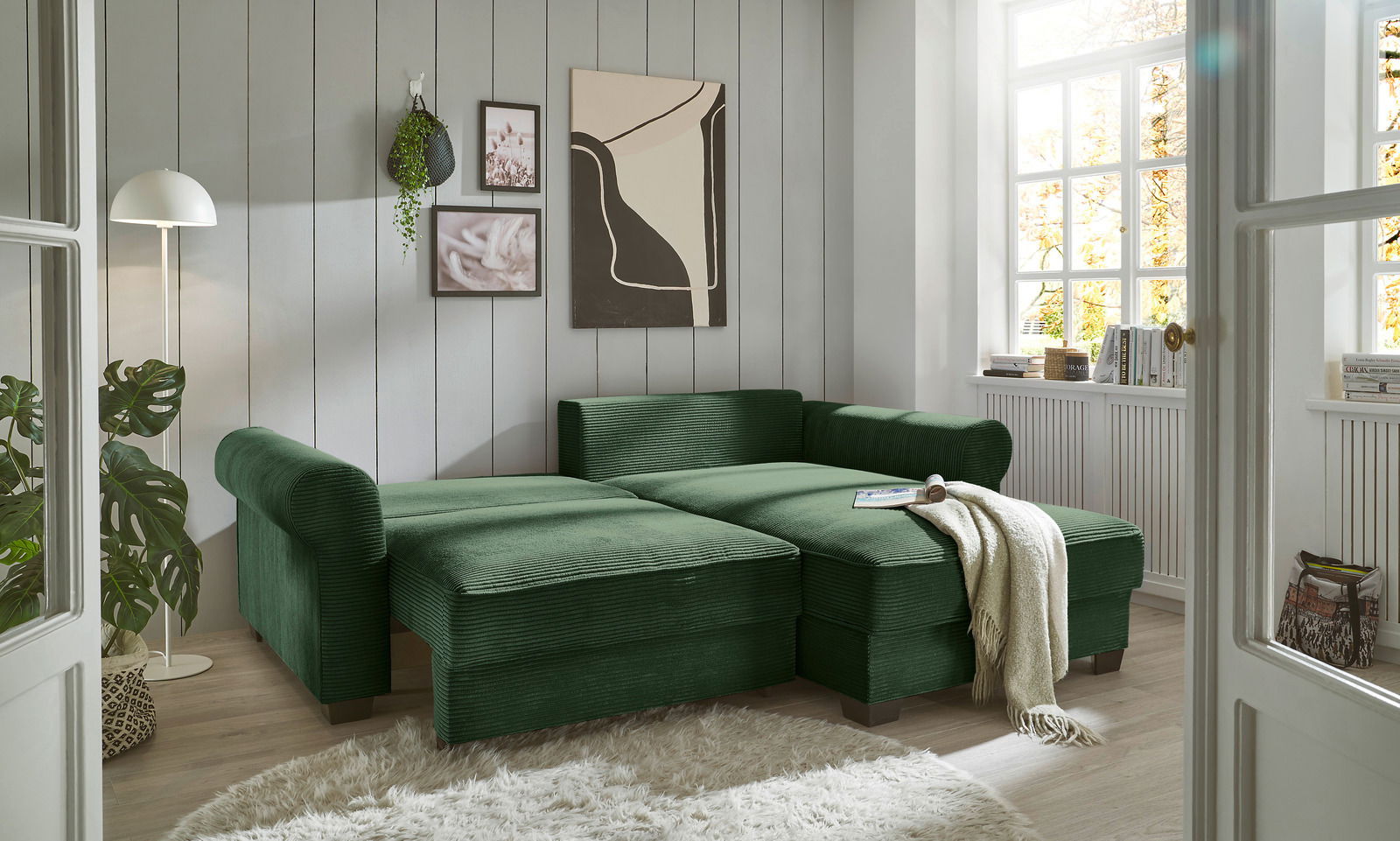 Grüne Rundecke in einem hellen Wohnzimmer mit großen Fenstern, aus der Perspektive von vorne links betrachtet.