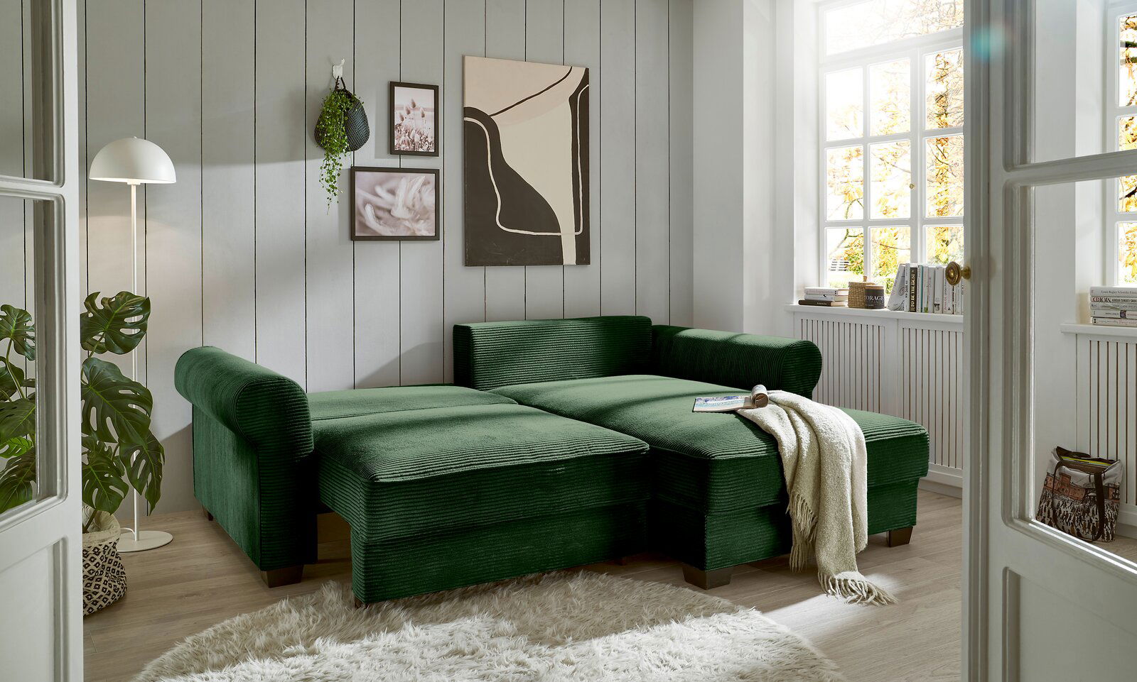 Grüne Rundecke in einem hellen Wohnzimmer mit großen Fenstern, aus der Perspektive von vorne links betrachtet.