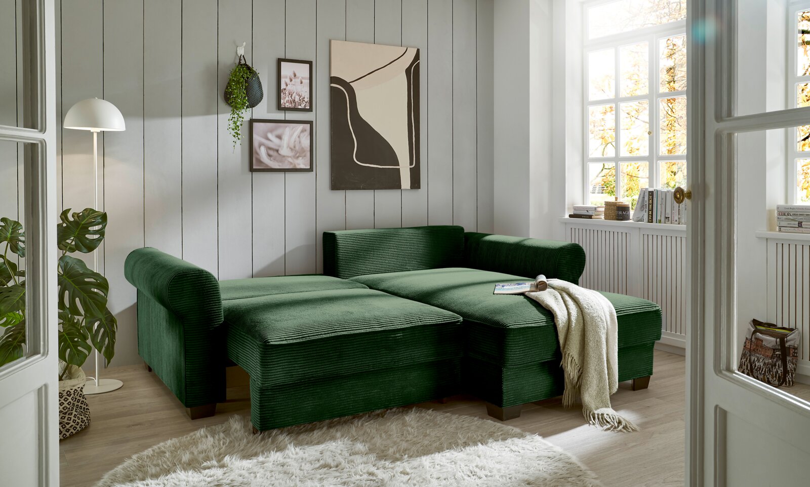 Grüne Rundecke in einem hellen Wohnzimmer mit großen Fenstern, aus der Perspektive von vorne links betrachtet.