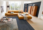 Moderne Longchairkombination in einem hellen Wohnzimmer mit großen Fenstern, aus der Perspektive von vorne rechts aufgenommen.