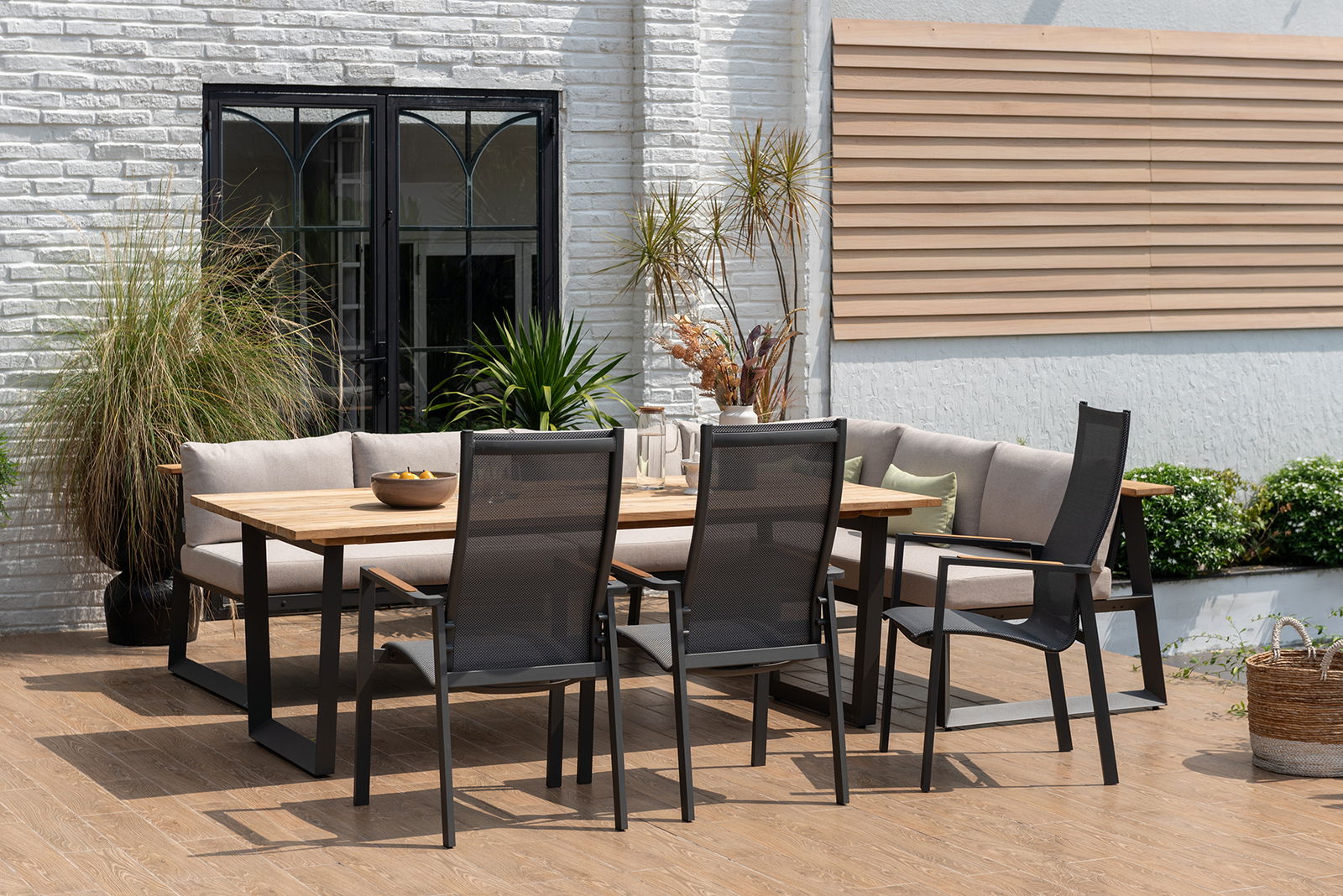Moderner Stapelsessel aus Metall und Netzgewebe, seitliche Perspektive auf einer Terrasse mit Holztisch und Pflanzen im Hintergrund.