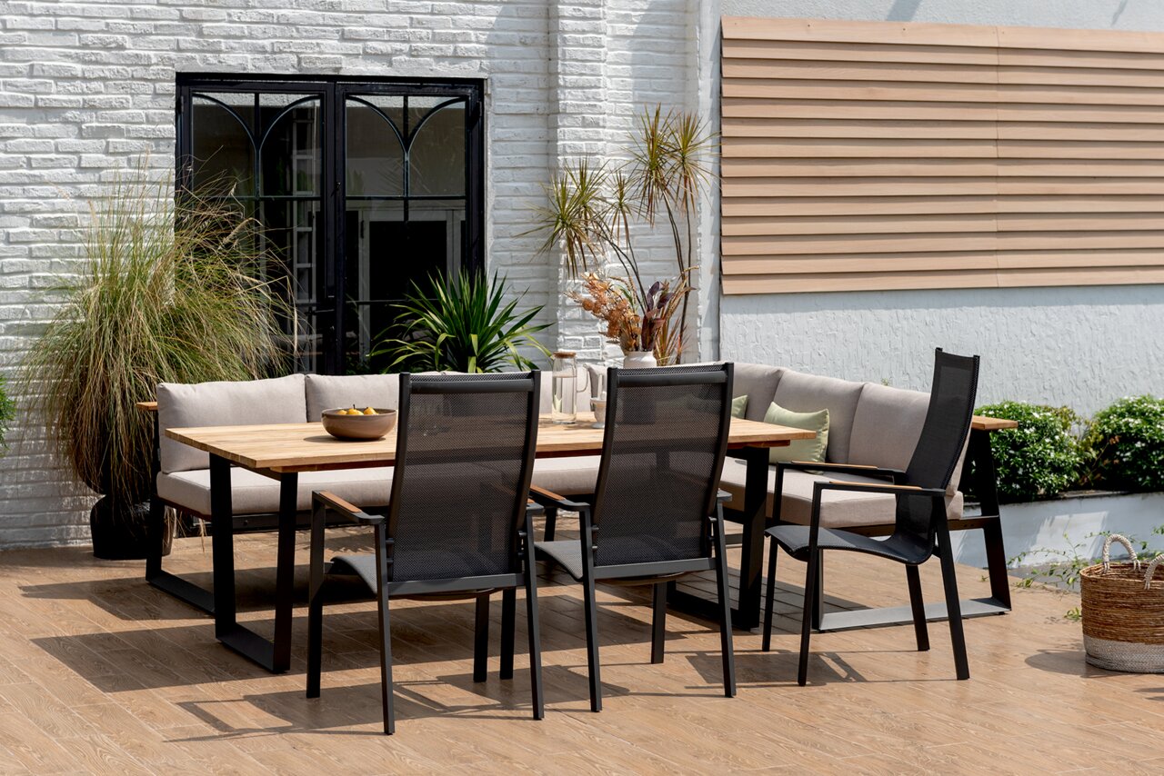 Moderne stapelstoel van metaal en gaas, zijaanzicht op een terras met een houten tafel en planten op de achtergrond.