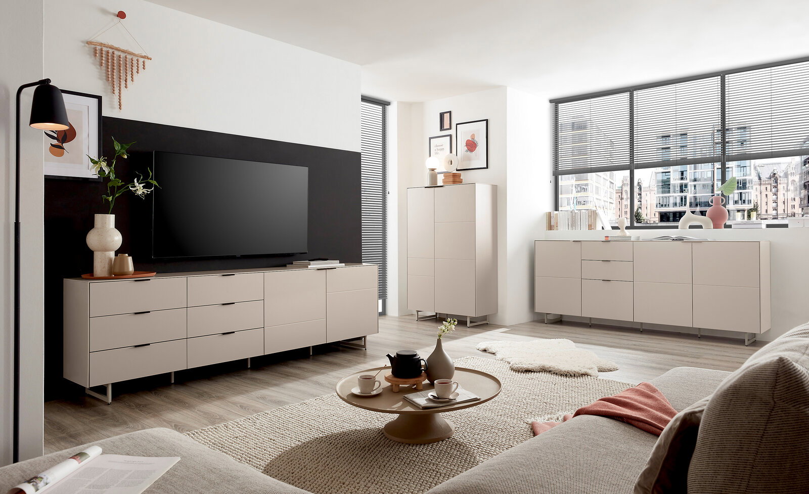 Z2 Highboard QUODA Modernes, helles Wohnzimmer mit beigen Sideboards und Highboard auf Metallfüßen, großem Fernseher an dunkler Akzentwand, Couchtisch und Sofa; Perspektive: Weitwinkelaufnahme aus Sitzhöhe schräg von vorne.