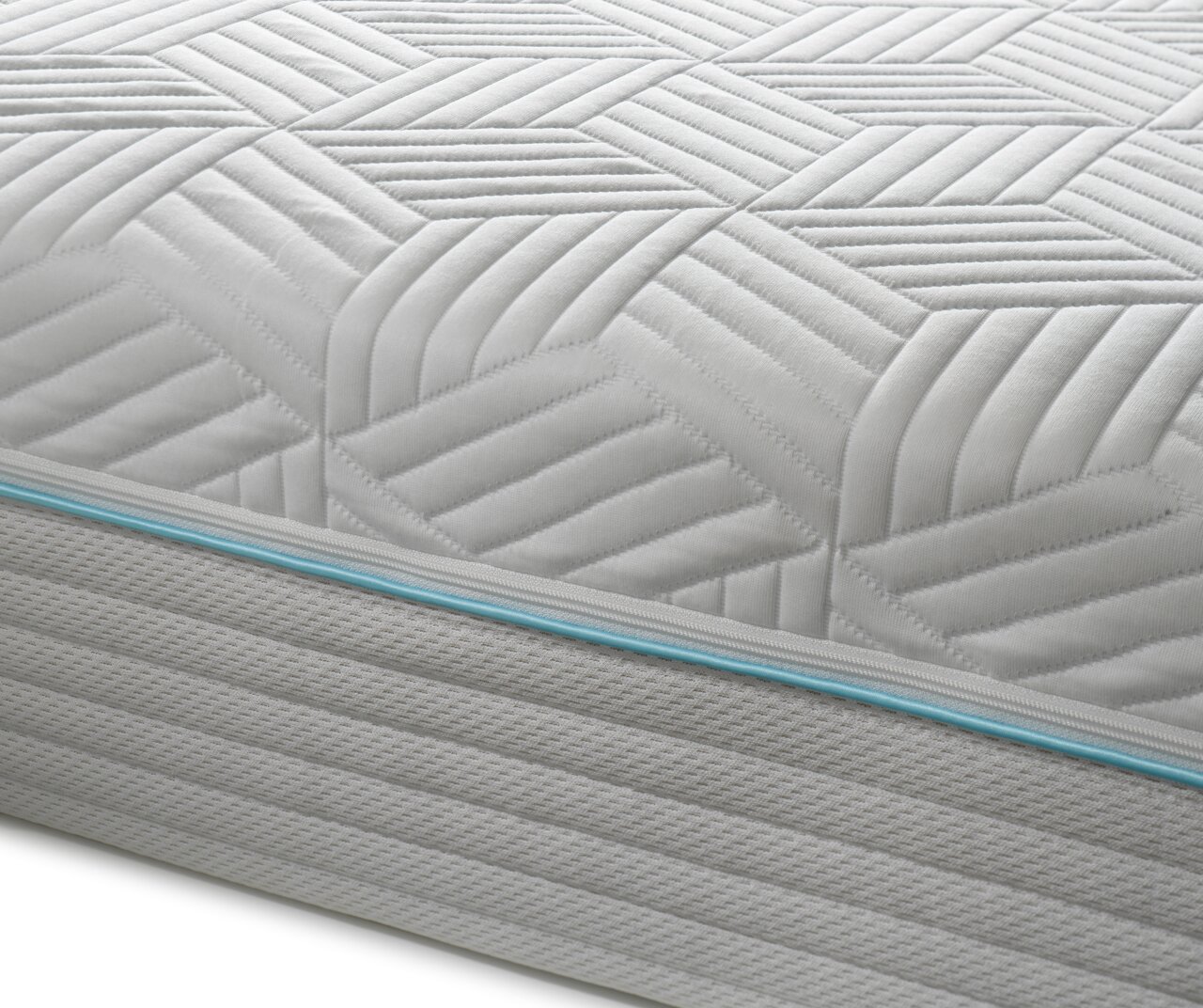 Nahaufnahme einer Gel-Kaltschaummatratze mit geometrischem Muster und blauer Ziernaht, seitliche Perspektive.