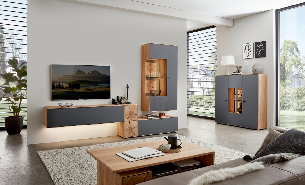 Moderne Wohnzimmer-Wandkombination in Holz und Grau mit TV, Vitrine und Sideboard, seitliche Perspektive.