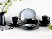 Elegantes 16-teiliges Kombiservice in Schwarz und Grau, bestehend aus Tellern, Tassen und Schalen, auf einem Tisch mit Blumenarrangement, aus frontaler Perspektive.